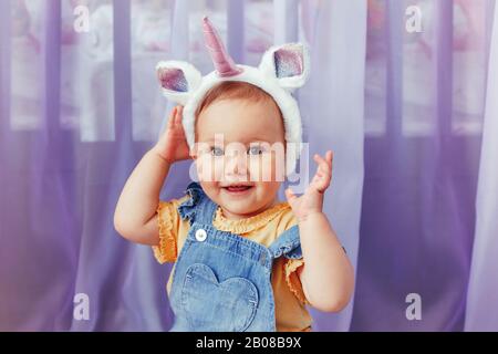 Süßes, liebenswürdig-kaukasisches Mädchen mit einhorn-Stirnband mit Horn und Ohren. Ziemlich lustige Kinder mit Kopfhaar märchenhaft tierisches Accessoire Spielzeug. Stockfoto