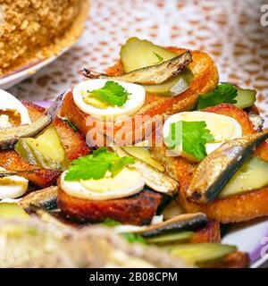 Sandwiches mit geräucherten Sprotten, gekochtes Ei, Essiggurken und Petersilie auf einem Teller. Selektiver Fokus Stockfoto