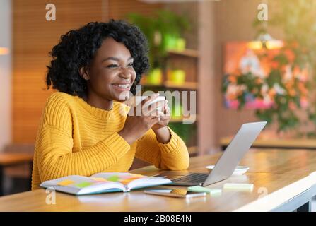 Aufgeregte Afro Mädchen, die Tee trinken, mit Laptop, Notizen machen Stockfoto