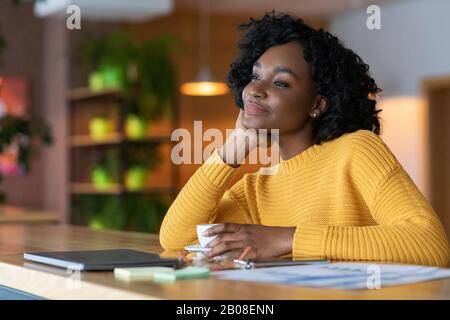 Entspannte Afro Mädchen, die während der Mittagspause eine Tasse Kaffee genießen Stockfoto