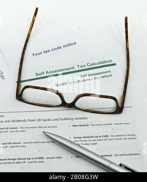 Nahaufnahme eines Steuerformulars zur Selbsteinschätzung mit einem Stift, einer Brille auf einem einfarbigen weißen Hintergrund Stockfoto