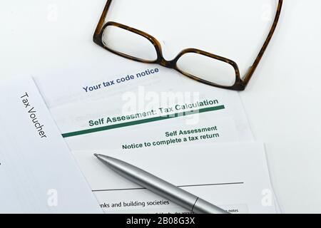 Nahaufnahme eines Steuerformulars zur Selbsteinschätzung mit einem Stift, einer Brille auf einem einfarbigen weißen Hintergrund Stockfoto