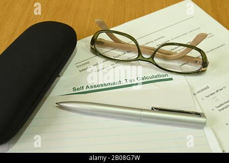 Nahaufnahme eines Steuerformulars zur Selbsteinschätzung mit einem Stift, einer Brille und einer Brille auf einem Holztisch Stockfoto