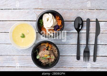 Verschiedene Arten Von Leckeren Fertiggerichten In Lebensmittelbehältern Auf Dem Tisch, Plastikmesser, Löffel und Gabel. Flaches Lay Stockfoto