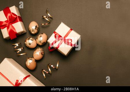 Goldene Eier mit Überraschungsgeschenkkästen auf dunklem Hintergrund. Rotes Band mit Schleifen. Festliche oster-komposition Stockfoto