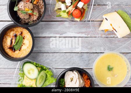 Fertiggerichte zum Essen in Essensboxen, Frühstück und Mittagessen. Tagesprogramm für Mahlzeiten. Mahlzeiten in schwarzen Behältern mit Besteck auf grauem Holztisch mitnehmen Stockfoto