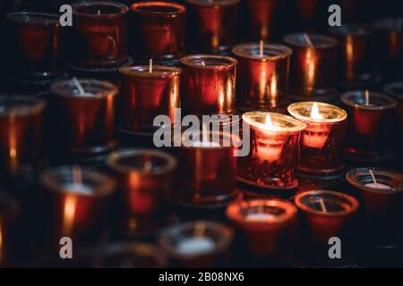 Zwei brennende Kerzen unter mehreren Reihen roter Kerzen in einer Kirche Stockfoto