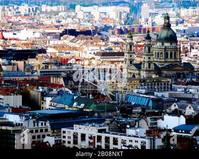 Blick auf das Zentrum von Budapest mit dichter Architektur und Dachflächen, Riesenrad, Stephansdom und Wohnhäusern. Beliebte Sehenswürdigkeiten Stockfoto