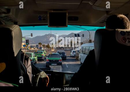 Aqaba, JORDANIEN - 30. JANUAR 2020: Auf grüne Ampelkreuzung warten. Taxis, Taxiwagen im Nahen Osten sind grün und schwarz lackiert. Blick vom Touristenbus. Sonniger Wintermorgen Stockfoto