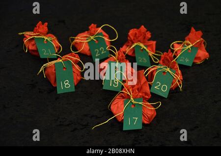 Vierundzwanzig kleine Geschenke in roten, grünen Tags eingewickelt goldene Zahlen von 1 bis 24 auf schwarz als selbstgemachter Adventskalender - 17. Dezember Stockfoto