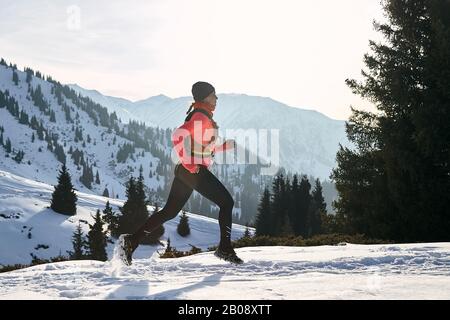 Der Trailrunner in pinkfarbener Jacke, Frau, die im Winter in den Bergen unterwegs ist, ist auf Schnee. Stockfoto