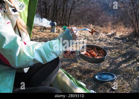 Nahaufnahme einer Frau in den Bergen im Zelt, die Pasta aus einem Topf in Brand isst Stockfoto