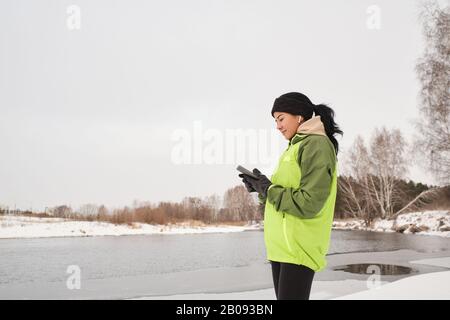 Inhalt attraktive weibliche Joggerin in Ohrstöpseln am Flussufer und Überprüfung der Fitness-App auf dem Telefon Stockfoto
