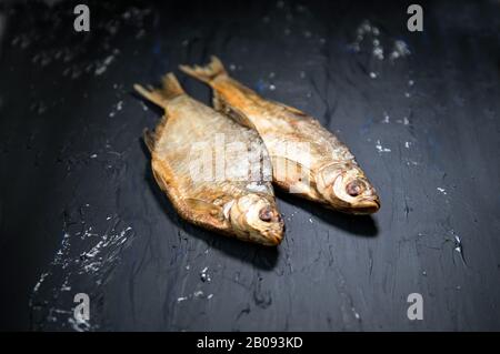 Gesalzene getrocknete Flussfische Makerel auf schwarzem Grund. Trockener gesalzter Fisch, Draufsicht, Kopierbereich. Traditioneller russischer Bier-Snack Stockfoto