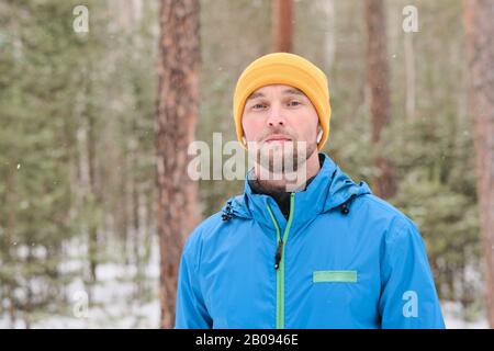 Porträt eines ernsthaften jungen Mannes in Ohrenknospen, der im Winterwald steht Stockfoto