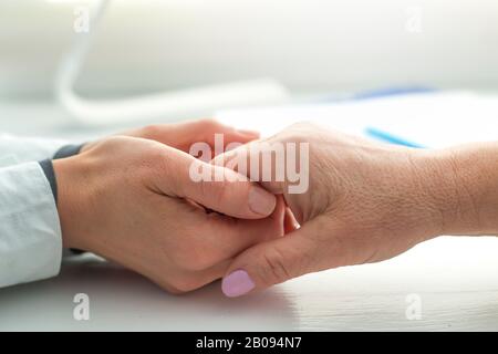 Der Arzt hält die Hand einer älteren Frau. Eine Krankenschwester unterstützt eine alte Patientin. Stockfoto