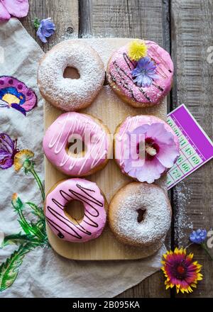 Pinkfarbene und weiße Donuts auf Holzbrett, flach, rustikal Stockfoto