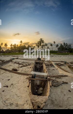 Traditionelles Holzboot bei Sonnenuntergang am tropischen Strand mit Palmen und weißem Sand am Strand von Diani, Watamu Kenia und Sansibar, Tansania Stockfoto