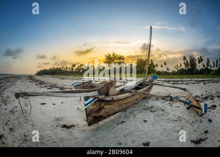 Traditionelles Holzboot bei Sonnenuntergang am tropischen Strand mit Palmen und weißem Sand am Strand von Diani, Watamu Kenia und Sansibar, Tansania Stockfoto