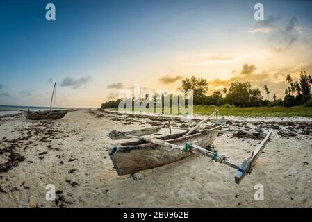 Traditionelles Holzboot bei Sonnenuntergang am tropischen Strand mit Palmen und weißem Sand am Strand von Diani, Watamu Kenia und Sansibar, Tansania Stockfoto
