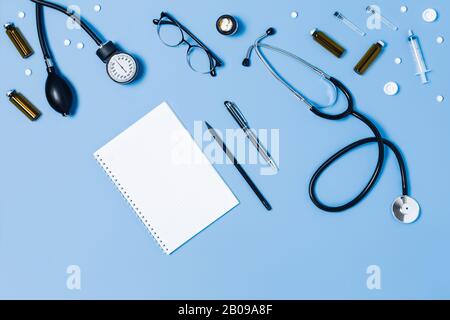 Medizinischer blauer Hintergrund mit verschiedenen Zubehörteilen: Stethoskop, Thermometer, Spritze und Tabletten. Stockfoto