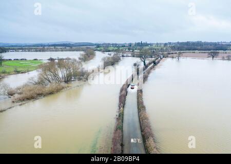 Auto, das durch die überflutete Straße am Fluss Severn in Shropshire, Großbritannien fährt Stockfoto