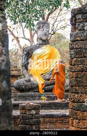 Ein buddhistischer Mönch in orangefarbenem Kleid betet vor einer alten Statue Stockfoto