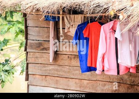 Hemden und andere Kleidungsstücke, die am Seil vor einem Holzhäuschen trocknen. Stockfoto
