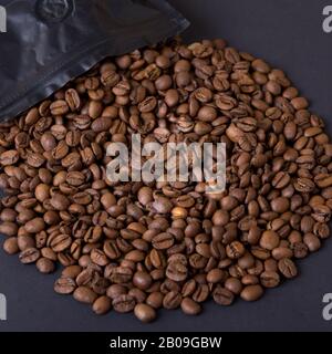 Kaffeebohnen verschütten sich aus einer schwarzen Packung. Kaffee-Hintergrund. Stockfoto