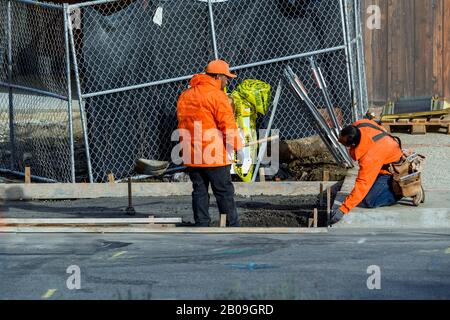 Betonbauunternehmer, die einen Gehweg, eine Bordsteinkante und eine Sturmabflussrinne an einem neuen Hausbau installieren. Stockfoto