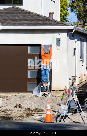 Bauarbeiter legen Klebeband auf eine Tür, um sie zu schützen, bevor sie an der Wand mit Stuck putzen. Renovierungshauskonzept. Stockfoto