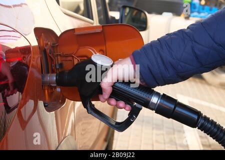 Mann füllt sein orangefarbenes Auto an der Tankstelle mit Benzin. Tankstellenpumpe. Zum Befüllen des Fahrzeugs mit Dieselkraftstoff. Stockfoto