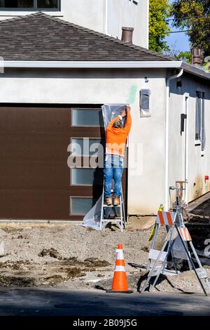 Bauarbeiter legen Klebeband auf eine Tür, um sie zu schützen, bevor sie an der Wand mit Stuck putzen. Renovierungshauskonzept. Stockfoto