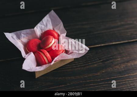 Rote französische Makronen in einer Schachtel auf dunklem Holztisch. Platz für Text. Stockfoto