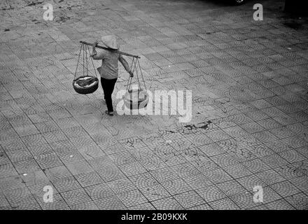Eine Frau trägt "Don ganh", zwei Körbe, die von jedem Ende eines Bambusmastes auf der Straße in Hanoi, Vietnam, entfernt sind. September 2011. Stockfoto