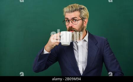 Mittagszeit für Lehrer. Kaffeesüchtig. Energieaufladung für den ganzen Tag. Koffeindosis. Lehrer in der Brille trinken Kaffee Kelkboard Hintergrund. Optimistisches Konzept. Angenehmer Schluck. Kaffeepause und Entspannung. Stockfoto