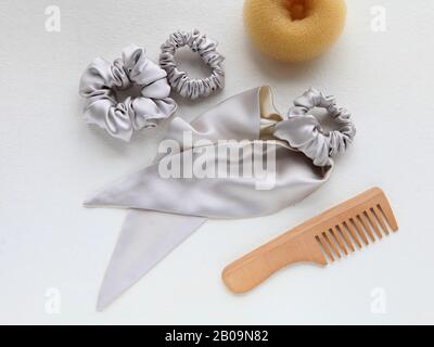 Haarbürste aus Holz, Barrette und Seide Scrunchy isoliert auf weiß. Flat Lay Frisierwerkzeuge und Accessoires Color Hair Scrunchies, Elastisches Haar Stockfoto