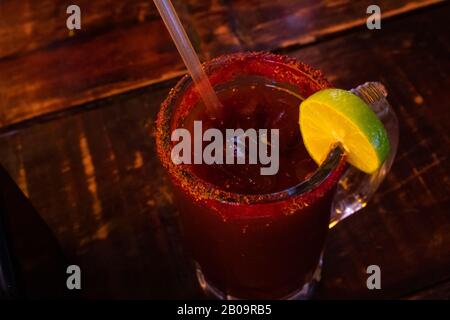 Köstliche rote Michelada mit mexikanischem Bier und Eis, serviert in einem großen Krug, der von der Hand einer Frau gehalten wird Stockfoto