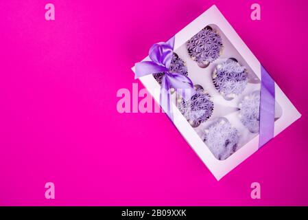 Köstliche schäubkuchen mit Quark in Form von Blumen auf pinkfarbenem Hintergrund. Weiße Cupcake-Verpackung. Stockfoto