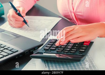 Nahaufnahme der Hände einer Buchhalterin, die mit einem Taschenrechner Rechnungen prüft. Gewinnanalyse, Berechnung von Steuern und Zahlungen, Business Concep Stockfoto