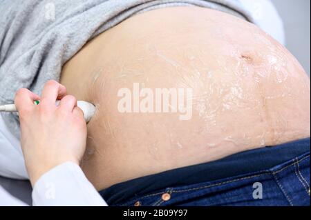 Der Arzt führt Ultraschall- oder Sonogramm-Verfahren an eine Schwangere Frau im Krankenhaus durch, Nahaufnahme des Geburtshelferaufnehmers, Der Den Schwinger auf dem Bauch der Zukünftigen Mutter bewegt. Stockfoto