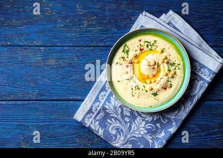 Kichererbsenhummus in einer hellblauen Schüssel auf einer blauen Serviette auf dunkelblauem Holzhintergrund Stockfoto