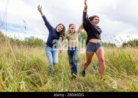 Sommerferien Urlaub glückliche Menschen Konzept. Gruppe von drei Freunden Junge und zwei Mädchen laufen und Spaß zusammen im Freien haben. Picknick mit Freunden auf dem Weg in die Natur Stockfoto