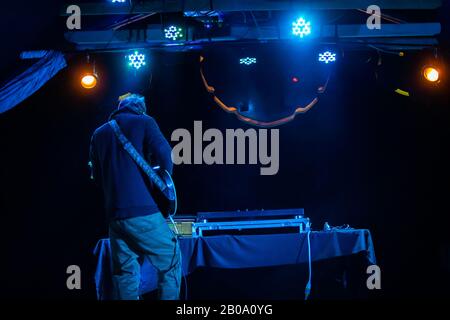 Ein weicher Blick von hinten auf einen Gitarristen, der nachts mit blauen Scheinwerfern auftrat, Musikinstrumente auf einem multikulturellen Festival spielte, kopiere Raum nach rechts Stockfoto