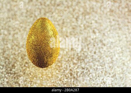 In der Luft hängt ein goldenes Ei. Auf einem strukturierten goldenen Hintergrund. Das Konzept zum Thema Ostern. Stockfoto