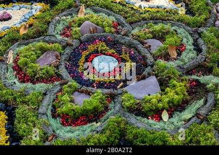 Ein Nahschuss kreativer Blumenkunst aus farbenfrohen, foraged Items aus einem Wald, großes Blumenmuster mit grünem Moos, roten Winterbeeren, Blattwerk Stockfoto