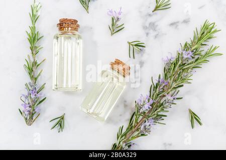 Rosmarin ätherisches Öl in Glasflasche und Zweige auf Marmortisch. Salvia Rosmarinus Öl. Draufsicht Stockfoto