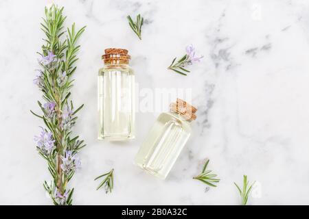 Rosmarin ätherisches Öl in Glasflasche und Zweige auf Marmortisch. Salvia Rosmarinus Öl. Draufsicht Stockfoto