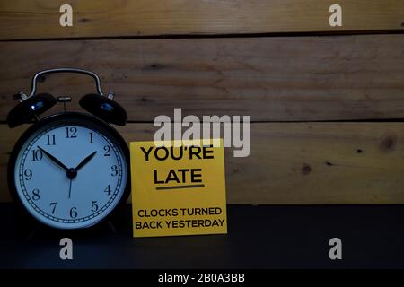 Sie sind Spät - Gestern Zurückgedrehte Uhren schreiben auf eine Haftnotiz, die auf Holzhintergrund isoliert ist. Stockfoto
