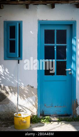 Traditioneller Eingang im zyprischen Haus mit blau geschlossener Tür, offenem Fenster und einem gelben Mopp Stockfoto